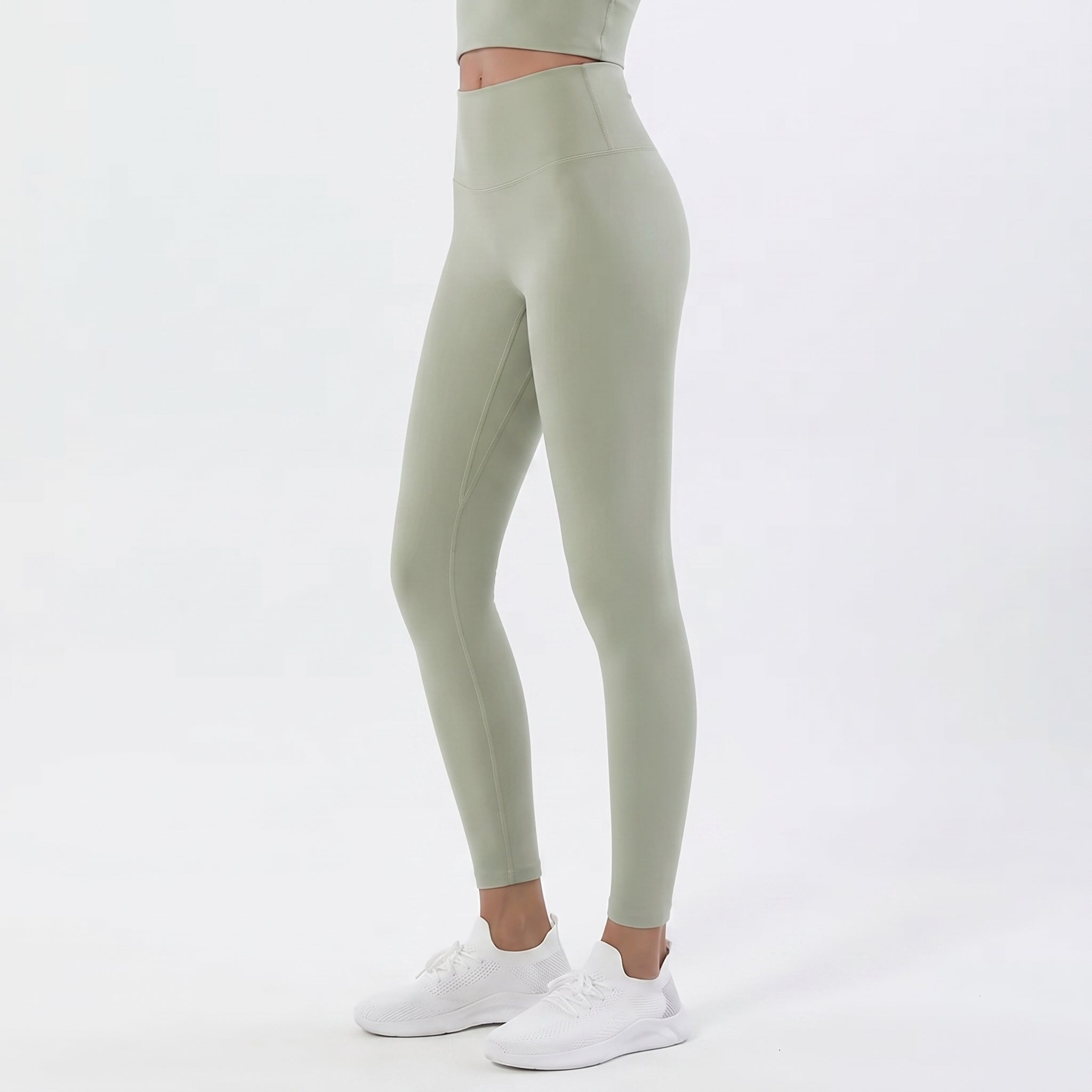 A model wearing sage green high-waisted leggings and white sneakers, shown from the waist down against a clean white studio background.
