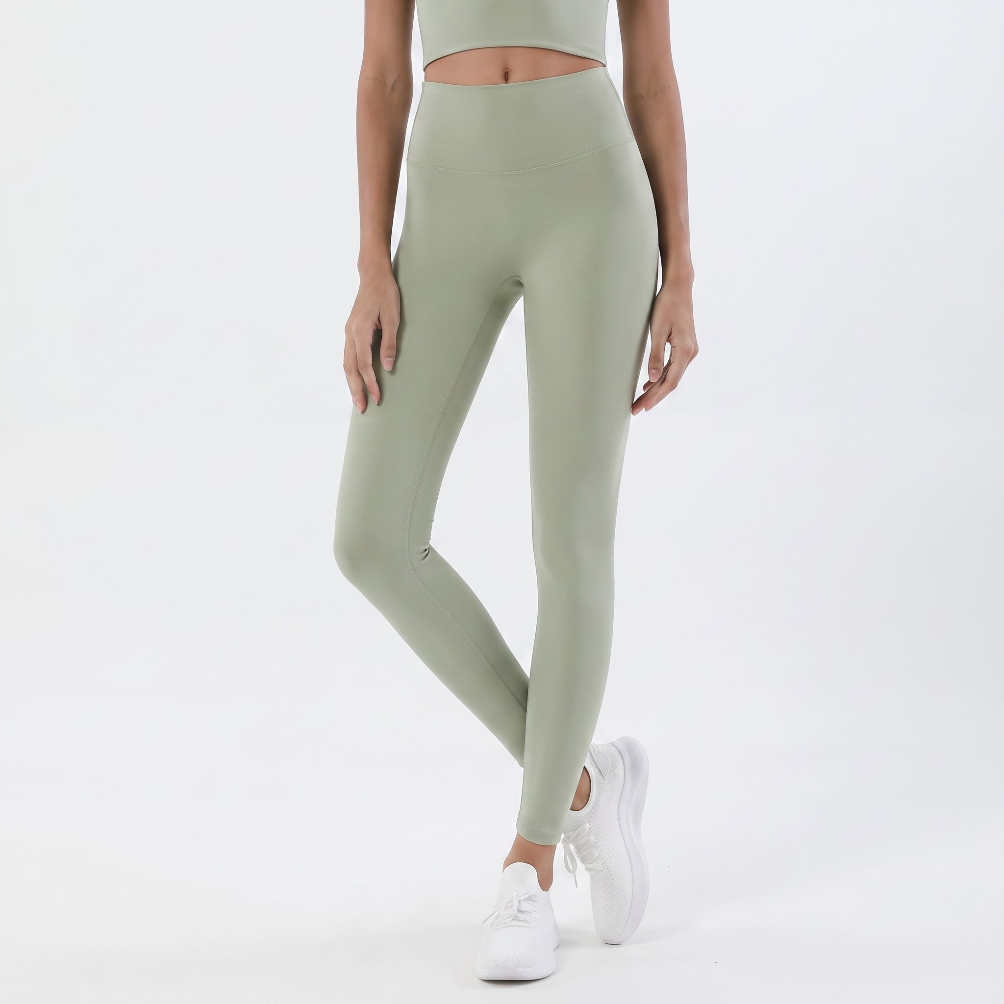 A model wearing high-waisted sage green leggings and white sneakers, shown from the waist down against a clean white studio background.