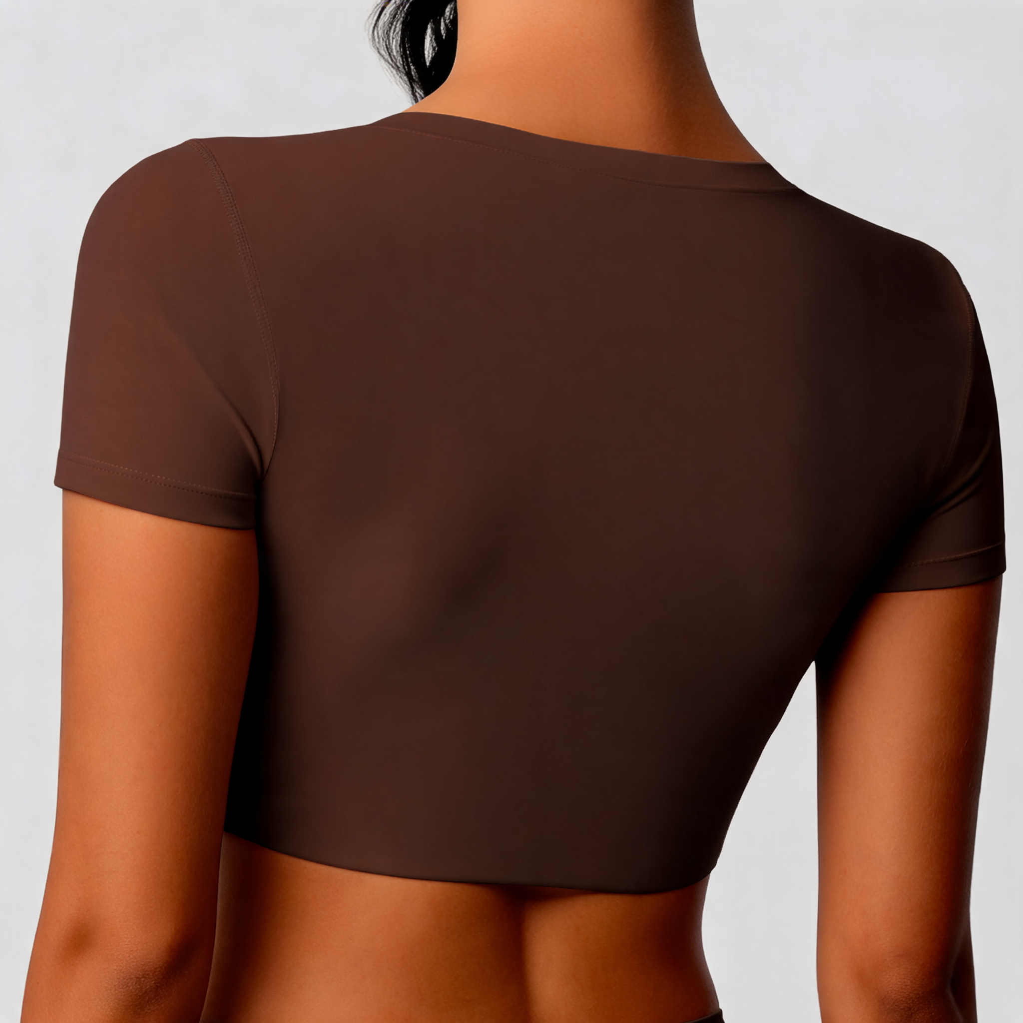 Rear view of a person wearing a short-sleeve cropped brown top against a light gray studio background.